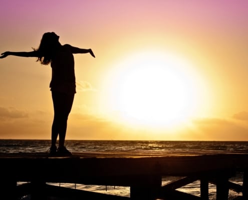 triumphant woman standing in front of sunset