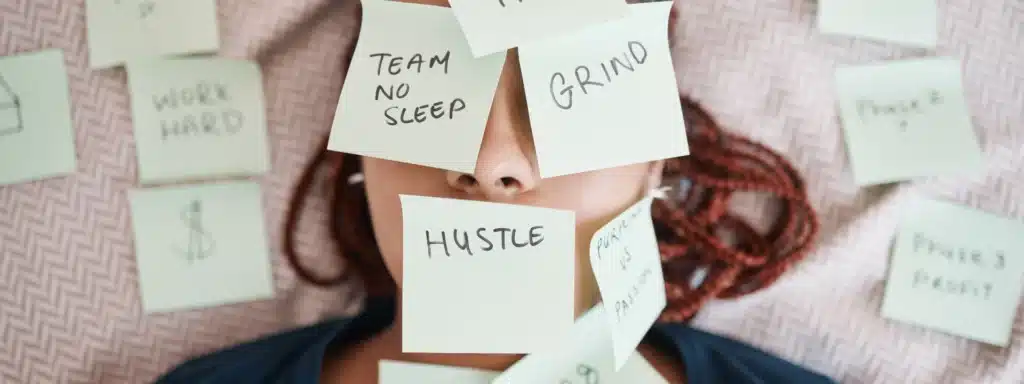 Overwhelmed adult woman lying down with sticky notes on face reading “Grind,” “Hustle,” and “No Sleep,” symbolizing the mental overload and pressure of adult ADHD.