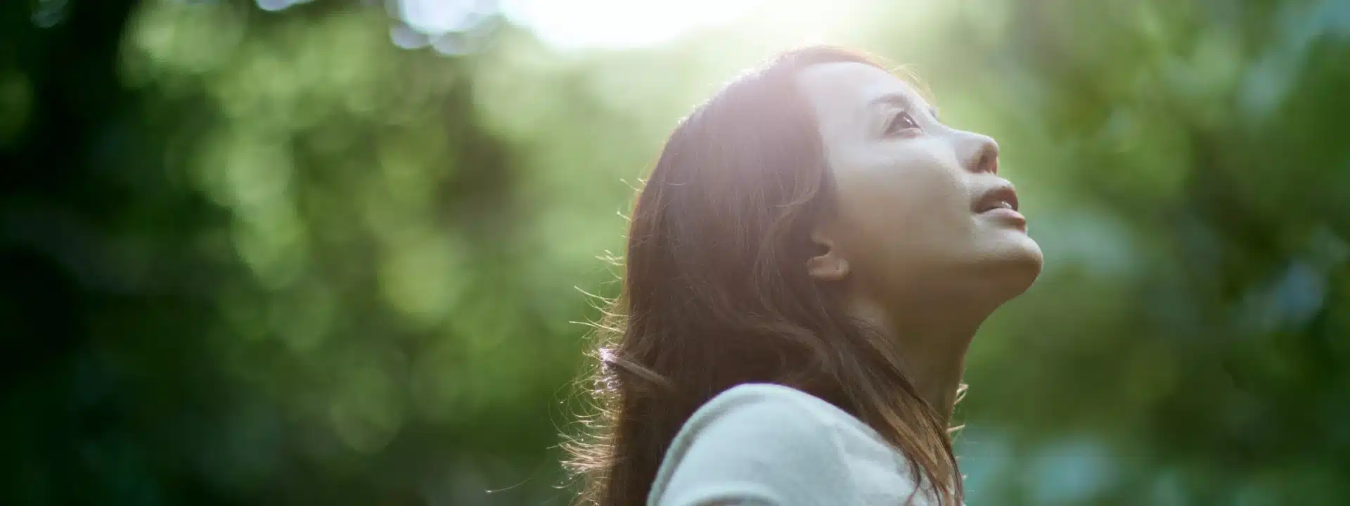 Woman standing in soft sunlight, looking upward in a peaceful forest setting—symbolizing healing, reflection, and hope after emotional abuse recovery.