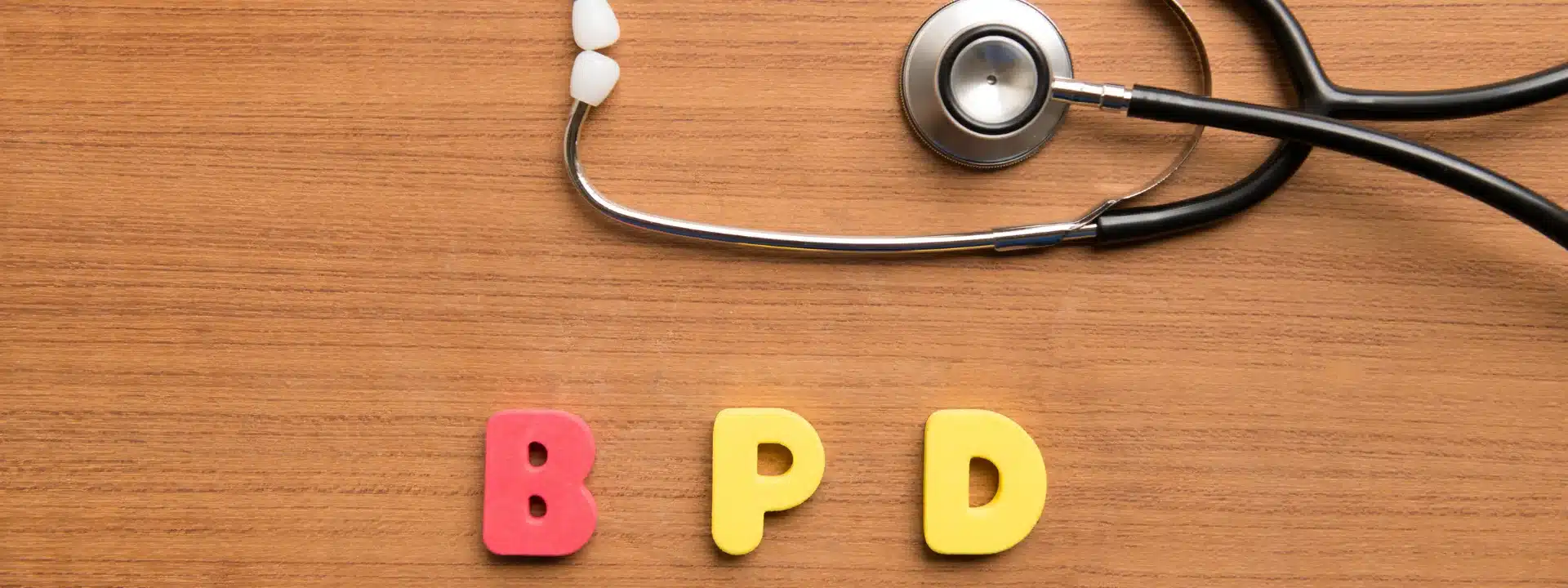 Colorful foam letters spelling “BPD” beside a stethoscope on a wood surface, symbolizing medical awareness and mental health treatment for borderline personality disorder.