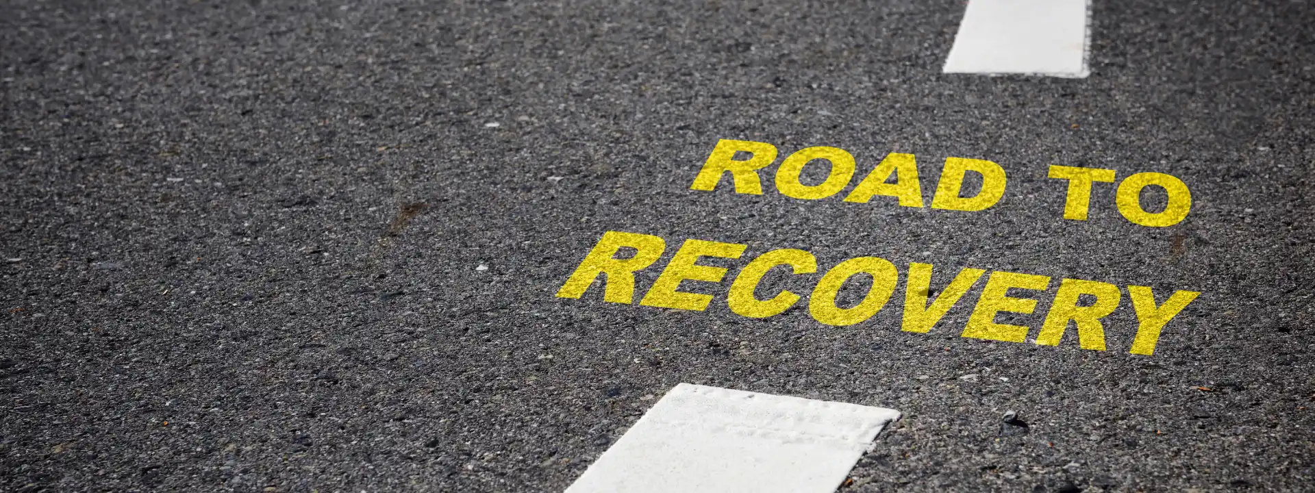 Yellow "Road to Recovery" text painted on asphalt, symbolizing the first steps toward healing from debilitating depression and finding hope through structured mental health care.