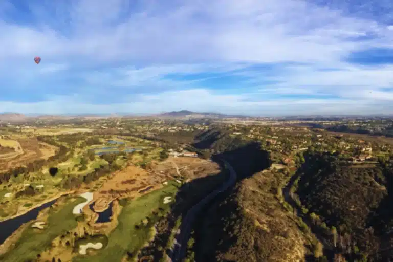 Aerial view of Rancho Santa Fe, California with golf courses, hills, and a winding road under a blue sky