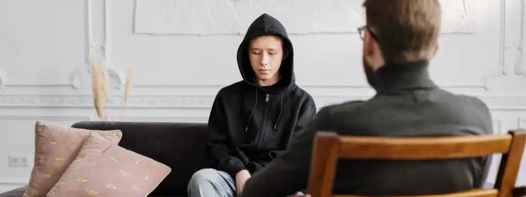 Person wearing a hoodie sitting across from a therapist during a counseling session at a crisis stabilization unit.