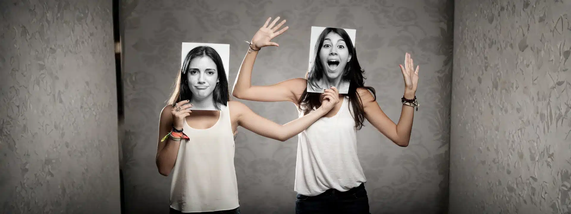 Two women holding photos of different facial expressions, symbolizing multiple identities and dissociation.