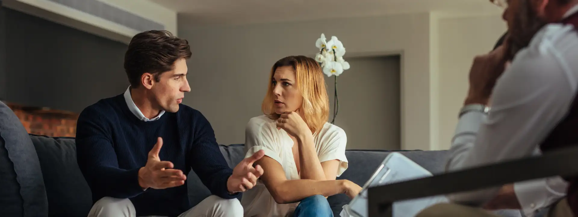A couple sitting together on a couch during a therapy session, speaking with a counselor.