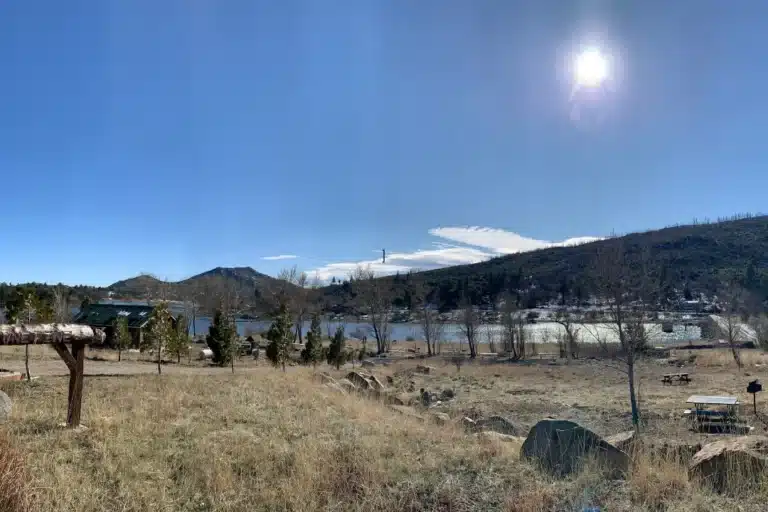 Alpine, California landscape with open grassland, scattered trees, rolling hills, and a bright sun shining in a clear blue sky.