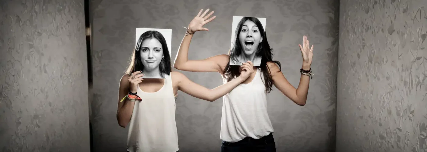 Two women holding photos of different facial expressions, symbolizing multiple identities and dissociation.