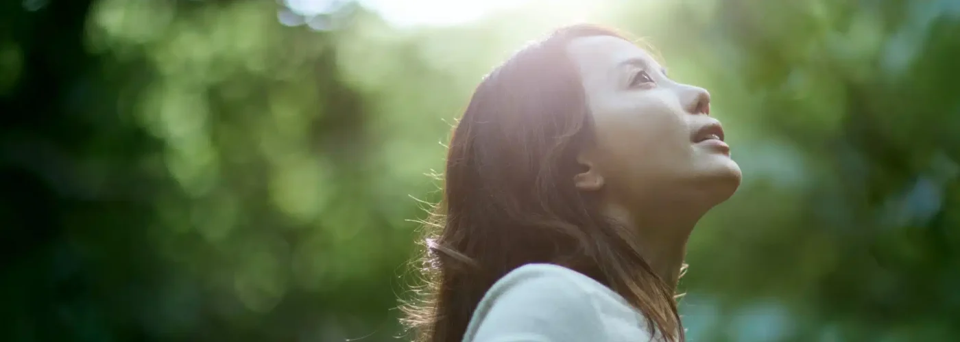 Woman standing in soft sunlight, looking upward in a peaceful forest setting—symbolizing healing, reflection, and hope after emotional abuse recovery.