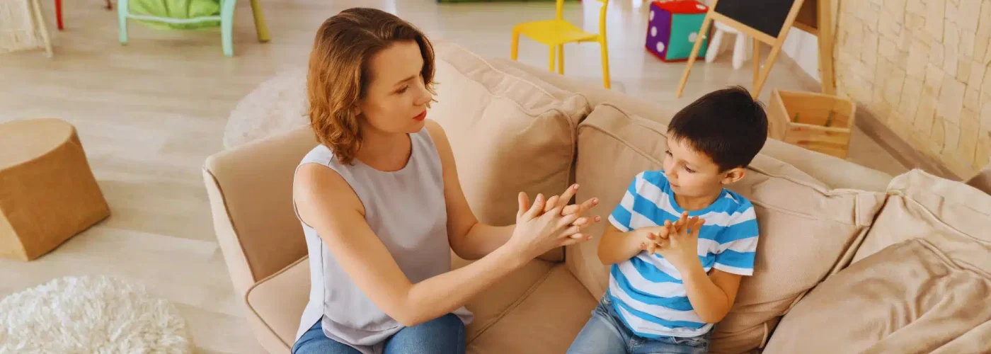 Therapist teaching a young boy with autism using hand exercises during a behavioral therapy session.