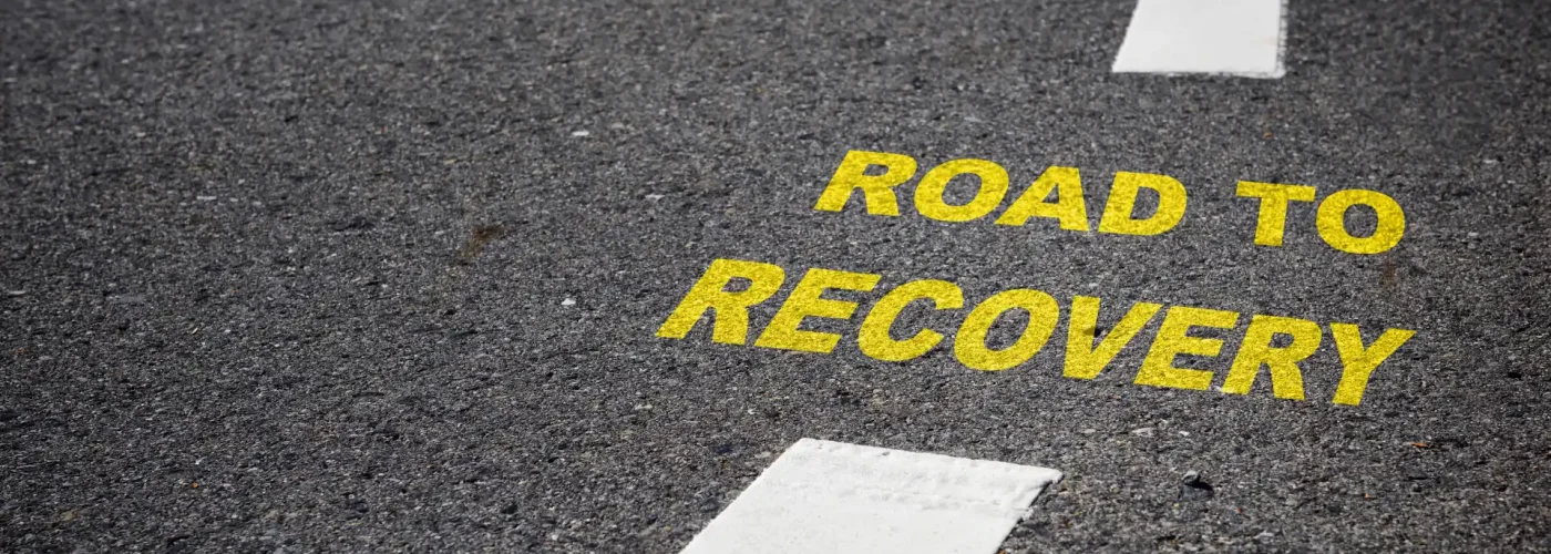 Yellow "Road to Recovery" text painted on asphalt, symbolizing the first steps toward healing from debilitating depression and finding hope through structured mental health care.